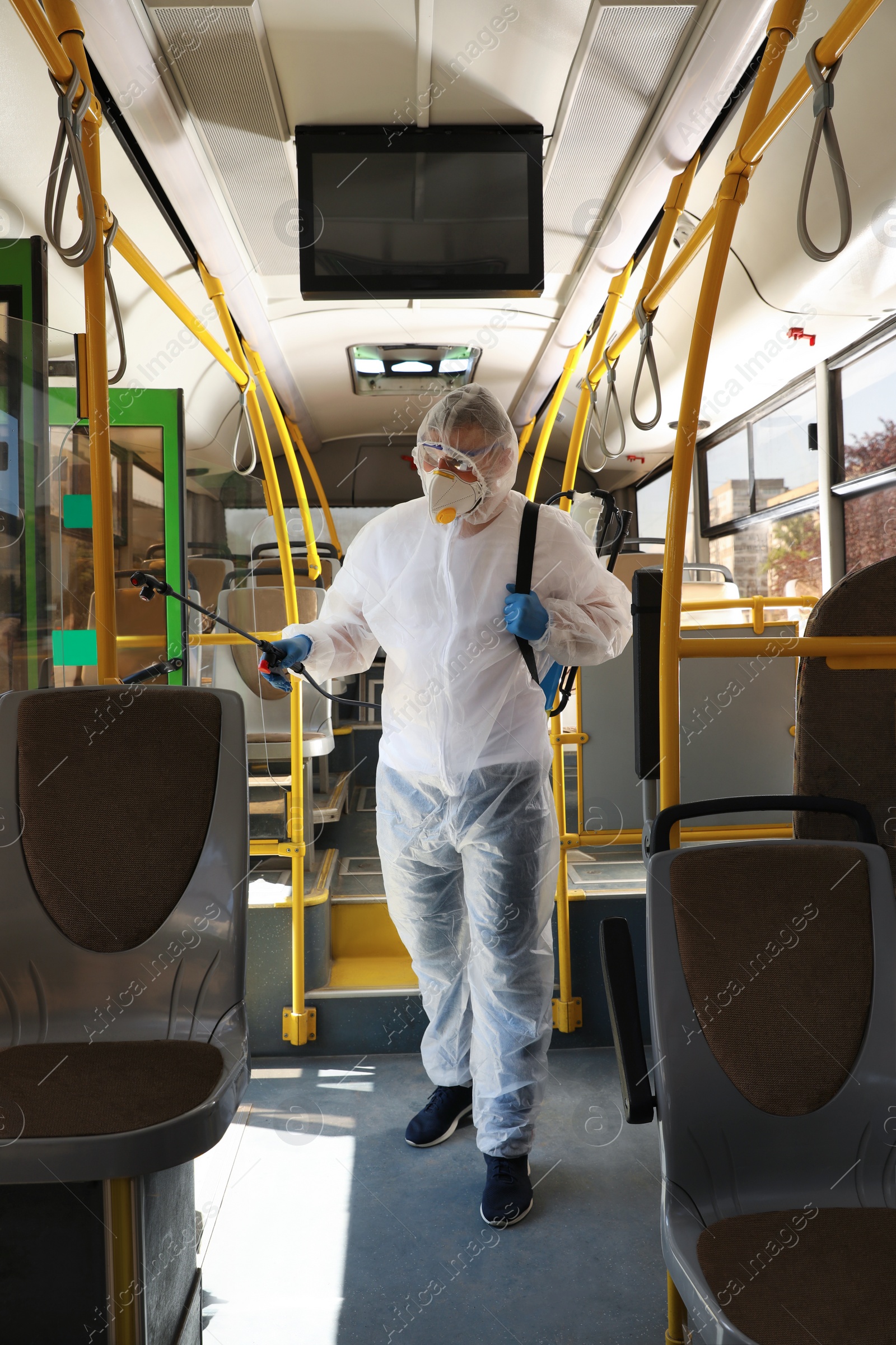 Photo of Public transport sanitation. Worker in protective suit disinfecting bus salon