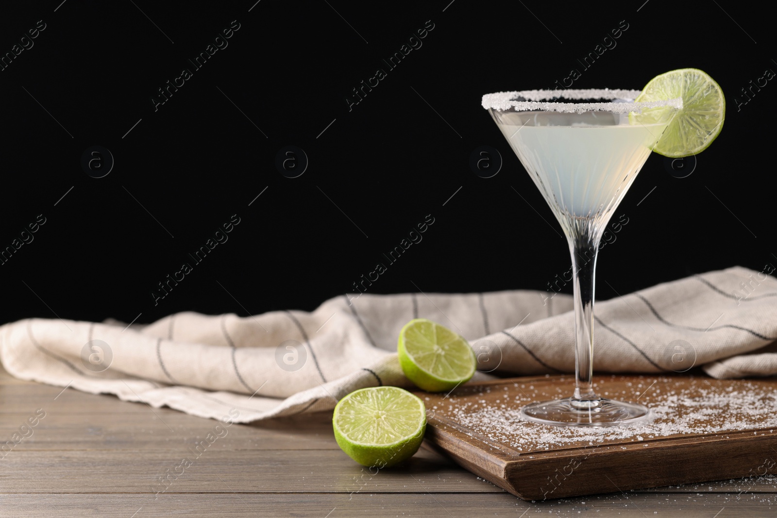 Photo of Martini glass of refreshing cocktail with lime and sugar on wooden table against black background. Space for text