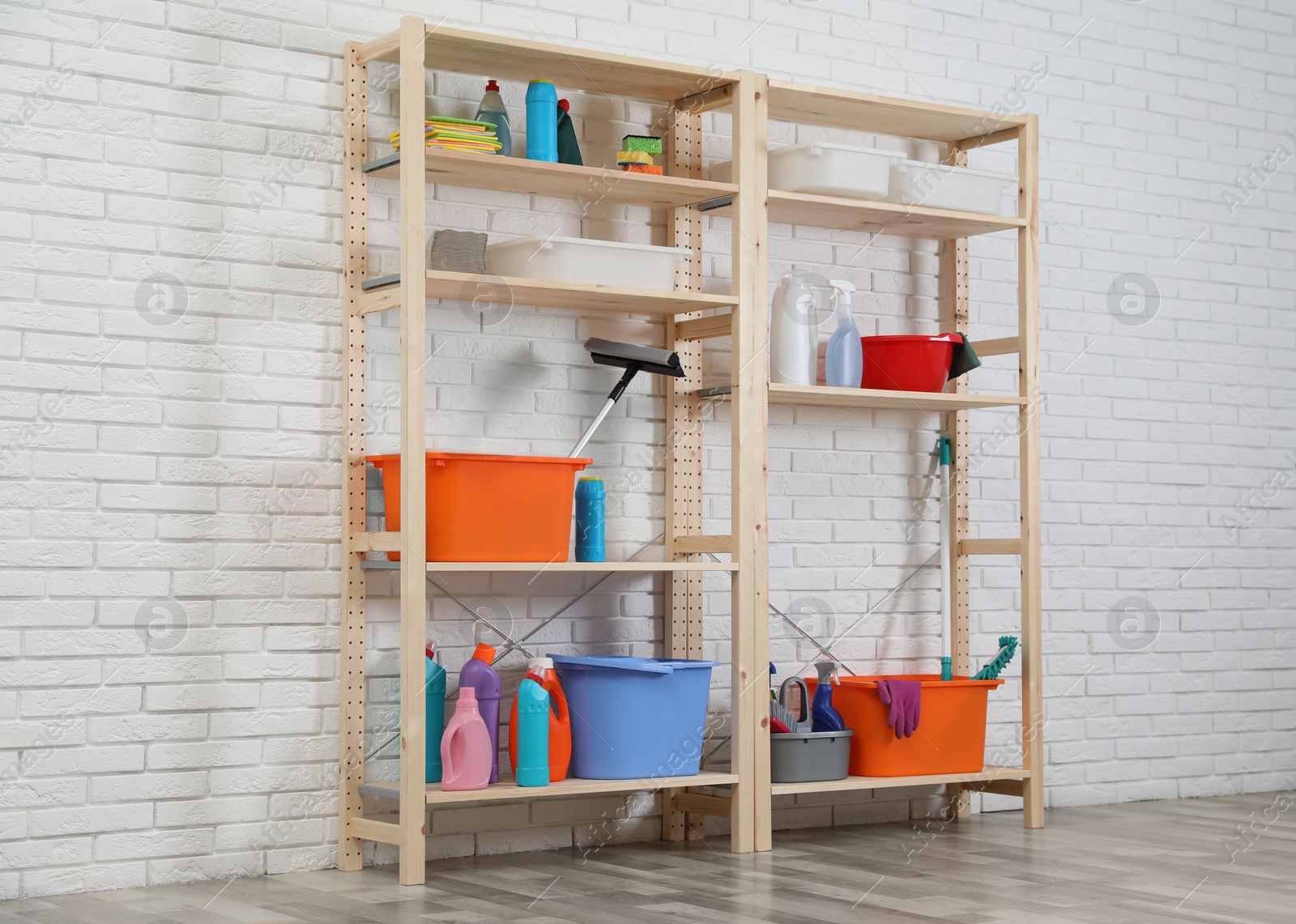 Photo of Wooden shelving units with cleaning equipment near white brick wall. Stylish room interior