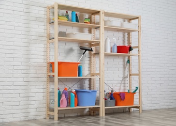 Wooden shelving units with cleaning equipment near white brick wall. Stylish room interior