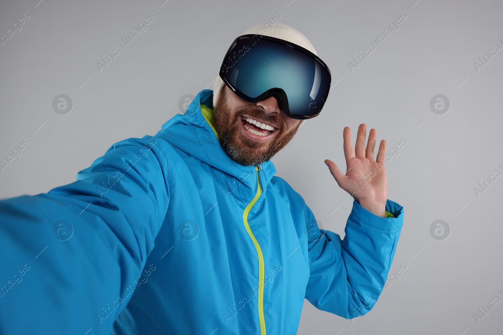 Photo of Winter sports. Happy man in ski suit and goggles taking selfie on gray background