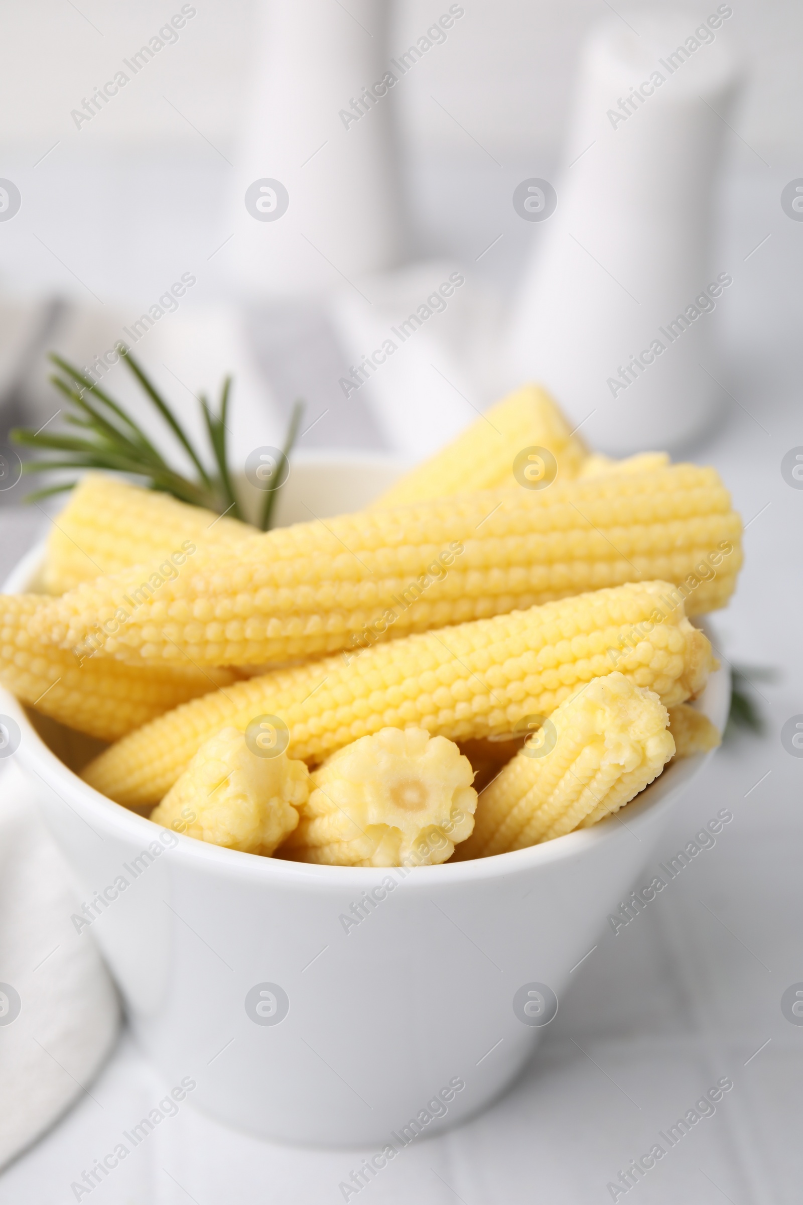 Photo of Tasty fresh yellow baby corns in bowl on white tiled table, closeup