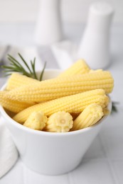 Photo of Tasty fresh yellow baby corns in bowl on white tiled table, closeup