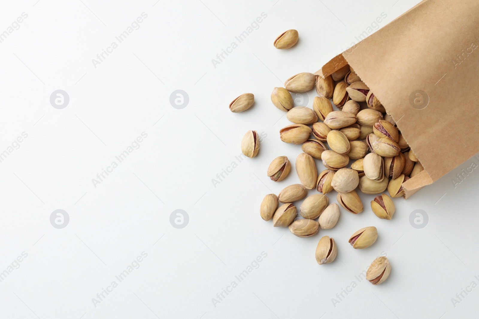 Photo of Overturned paper bag with pistachio nuts on white background, flat lay. Space for text