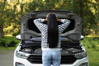 Photo of Young woman near broken car outdoors, back view