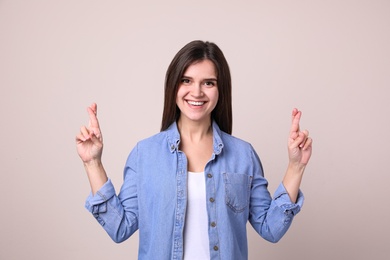 Photo of Happy young woman crossing fingers on light background. Dealing with stress