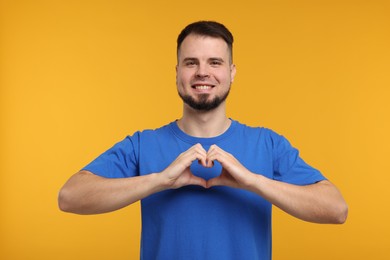 Photo of Man showing heart gesture with hands on golden background