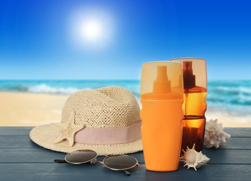Image of Bottles of skin sun protection products and beach accessories on blue wooden table against seascape. Space for design