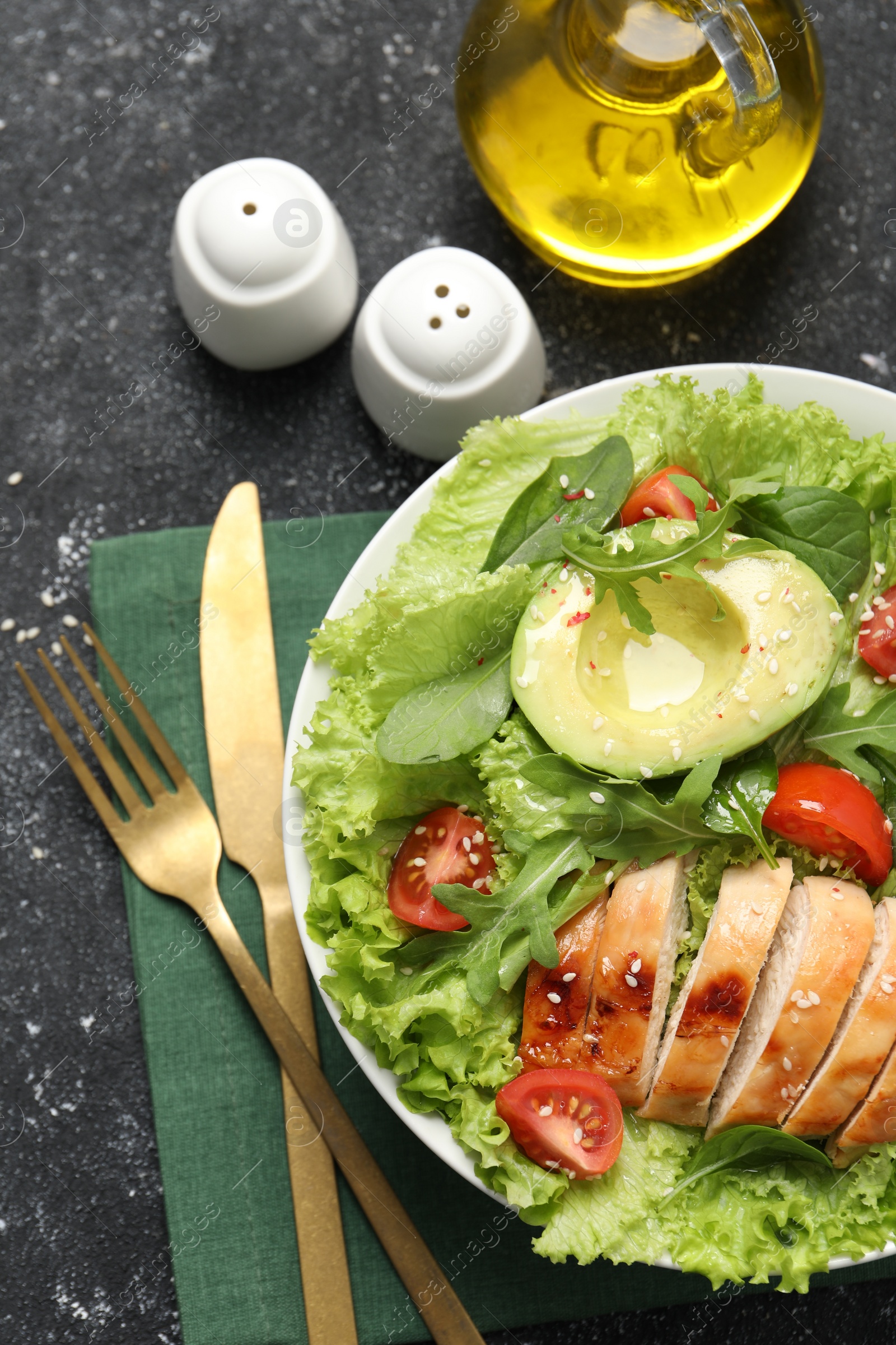 Photo of Delicious salad with chicken, cherry tomato and avocado served on grey textured table, flat lay