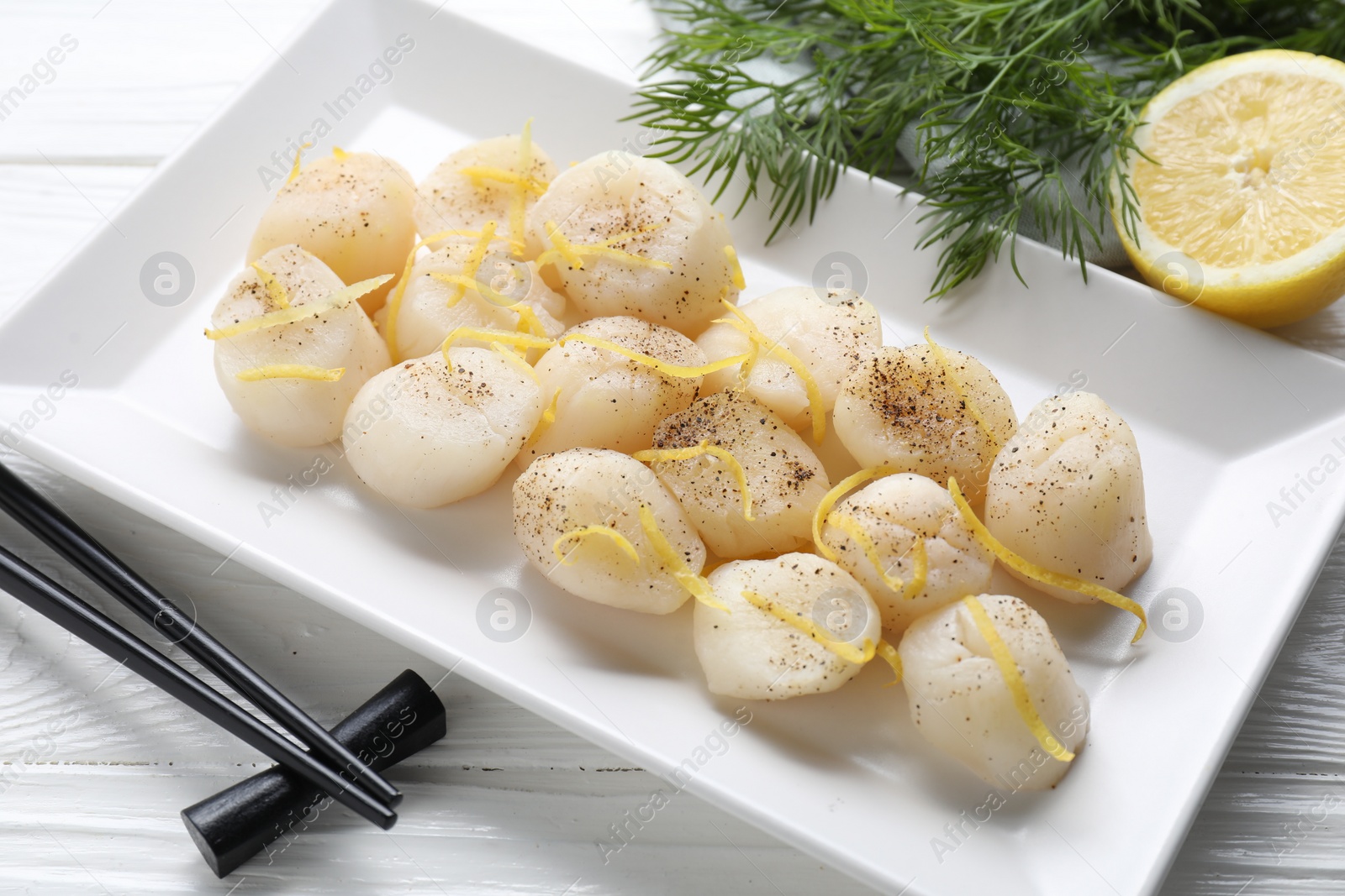 Photo of Raw scallops with milled pepper, lemon zest and dill on white wooden table, closeup