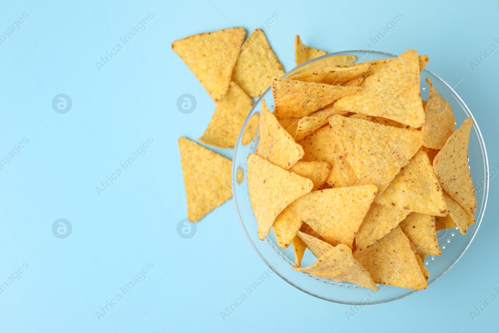 Photo of Glass bowl of tasty Mexican nachos chips on light blue background, top view