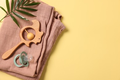Photo of Baby accessories. Wooden rattle, pacifier, palm leaf and cloth on yellow background, top view. Space for text