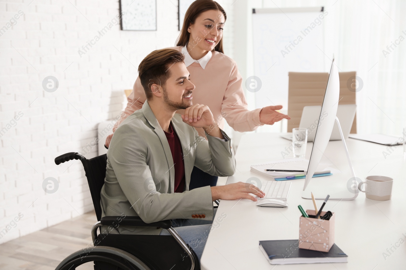 Photo of Man in wheelchair with his colleague at workplace