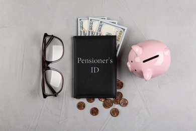 Photo of Pension certificate with American money, glasses and piggybank on grey stone table, flat lay