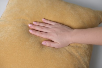 Woman touching soft yellow pillow on bed, closeup