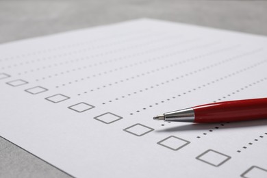 Paper sheet with checkboxes and pen on light grey table, closeup. Checklist