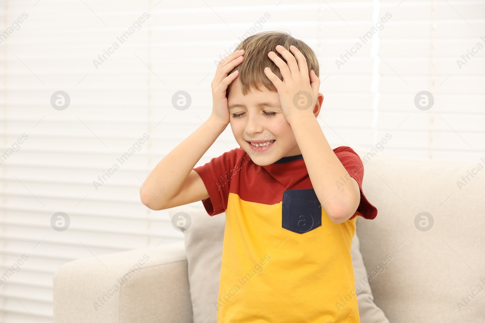 Photo of Little boy suffering from headache on sofa at home
