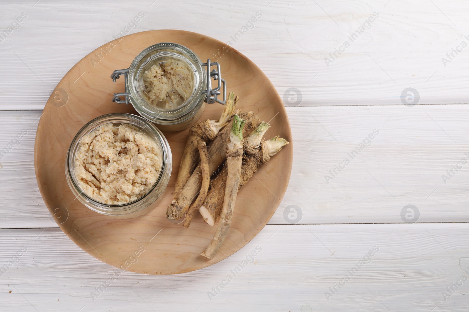 Photo of Platter with tasty prepared horseradish and roots on white wooden table, top view. Space for text