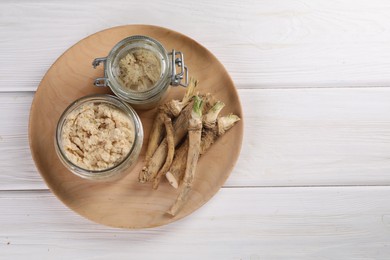 Photo of Platter with tasty prepared horseradish and roots on white wooden table, top view. Space for text
