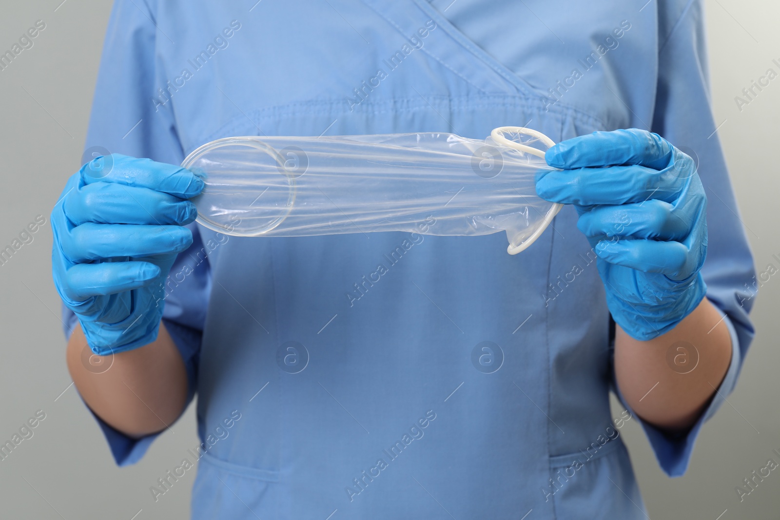 Photo of Doctor with unrolled female condom on light grey background, closeup. Safe sex