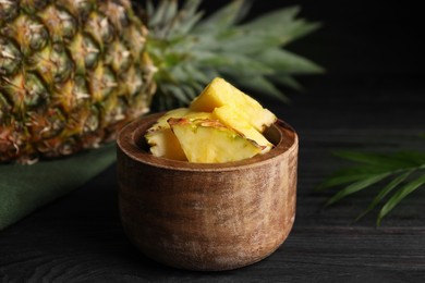 Photo of Pieces of tasty ripe pineapple in bowl on dark wooden table
