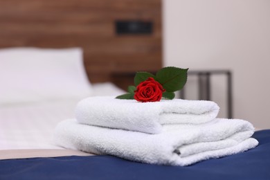 Photo of Stack of clean towels with flower on bed in hotel room