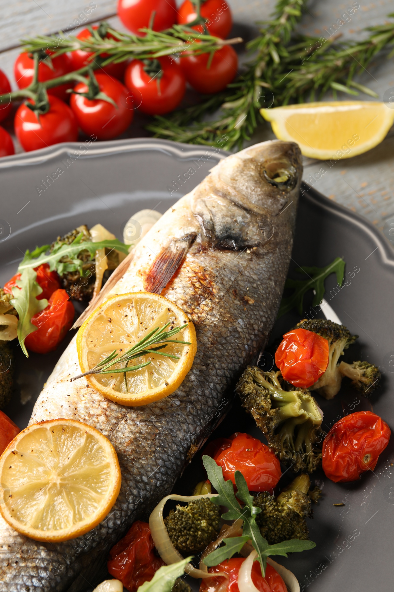 Photo of Baked fish with vegetables, rosemary and lemon on grey wooden table, closeup