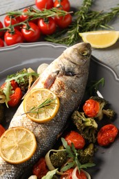 Baked fish with vegetables, rosemary and lemon on grey wooden table, closeup