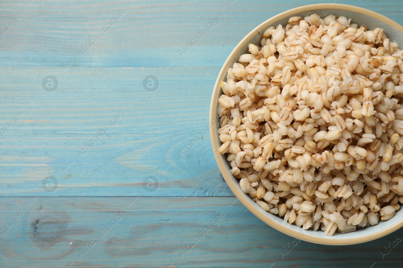 Photo of Delicious pearl barley in bowl on light blue wooden table, top view. Space for text