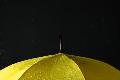 Photo of Opened yellow umbrella under rain against black background, closeup