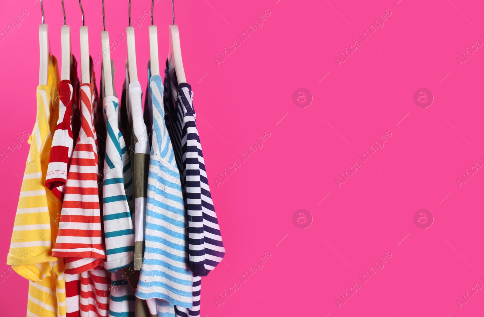 Photo of Colorful clothes on hangers against pink background, space for text