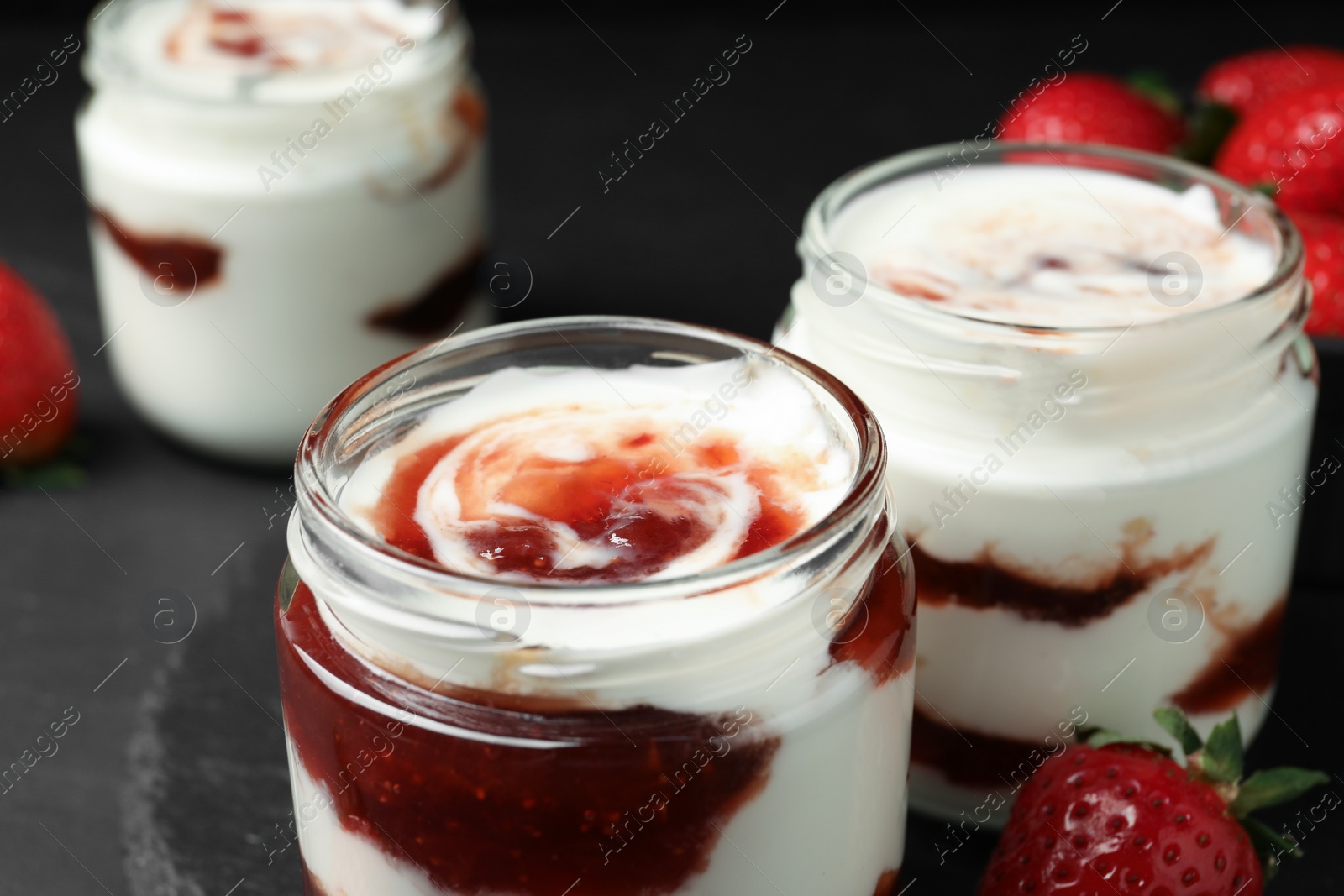 Photo of Tasty yoghurt with jam and strawberry on black table, closeup