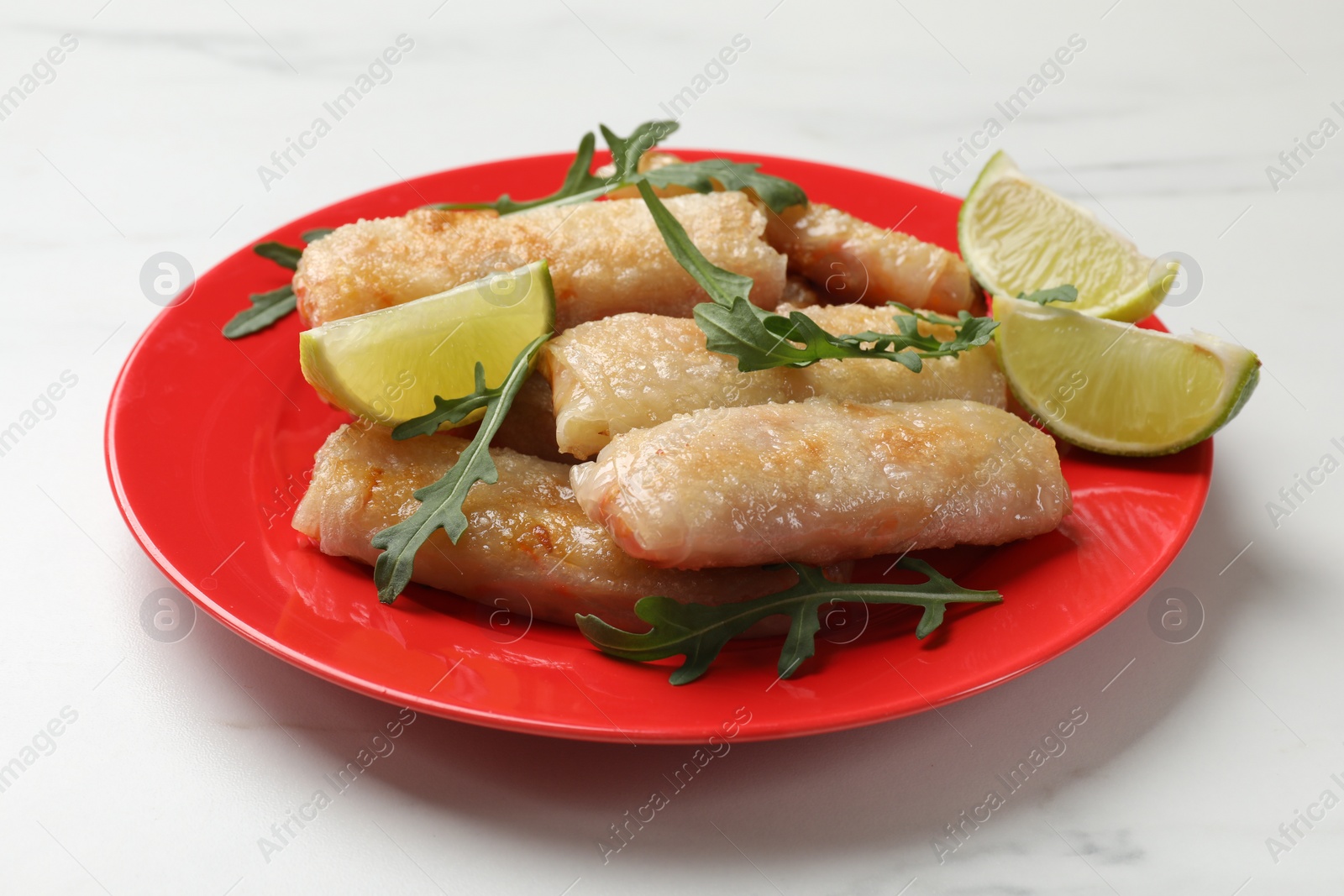 Photo of Plate with tasty fried spring rolls, arugula and lime on white table, closeup