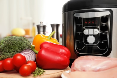 Photo of Modern multi cooker and products on table in kitchen, closeup. Space for text