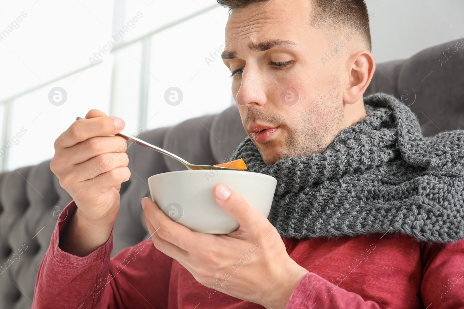 Photo of Sick young man eating broth to cure cold in bed at home