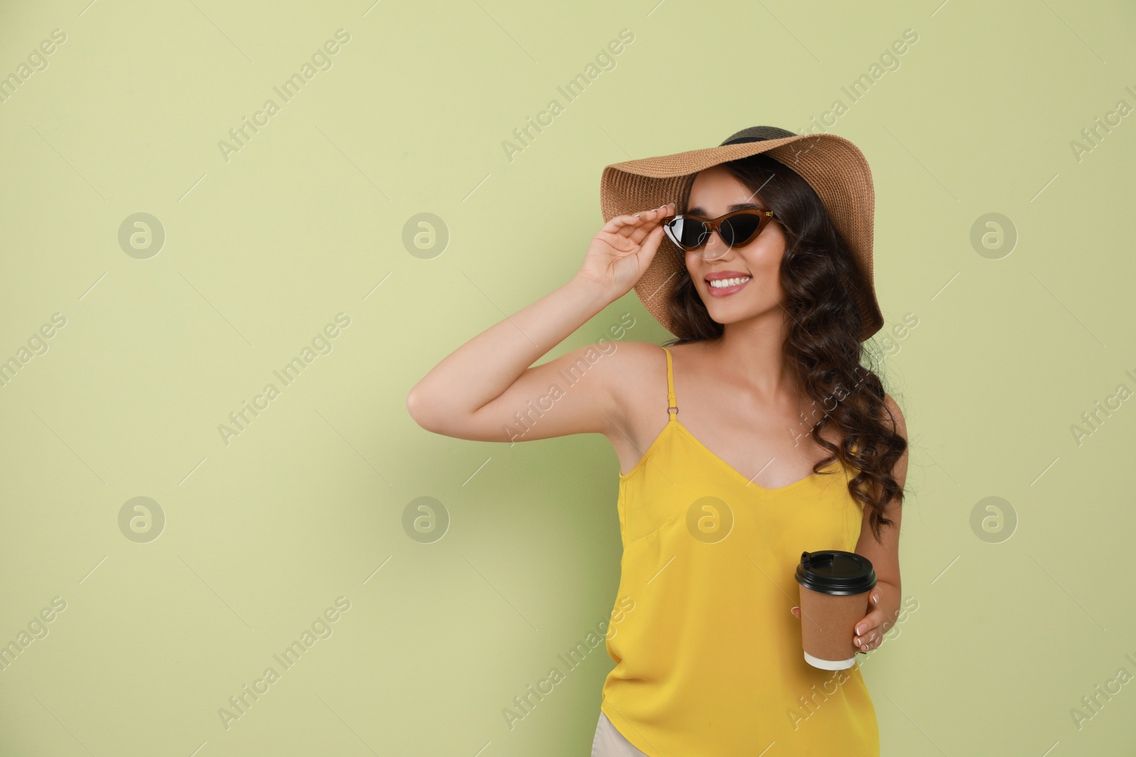 Photo of Beautiful young woman with straw hat and cup of coffee on light green background. Space for text