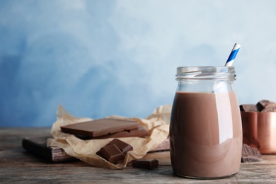 Photo of Jar with tasty chocolate milk on wooden table, space for text. Dairy drink