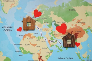 Photo of Paper hearts and markings between wooden house models on world map symbolizing connection in long-distance relationship, flat lay
