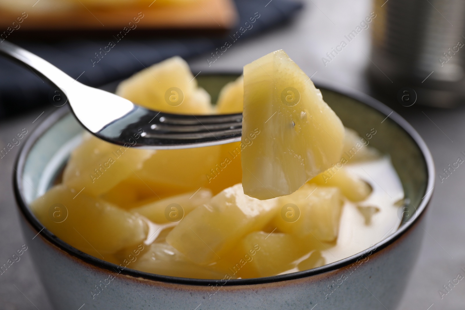 Photo of Fork with canned pineapple piece over bowl on table, closeup