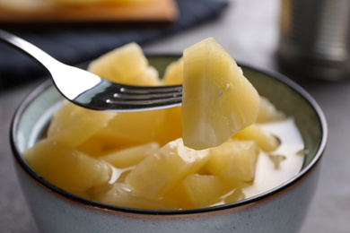 Photo of Fork with canned pineapple piece over bowl on table, closeup