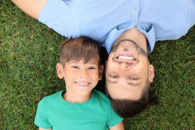 Father with his cute child on green grass in park, top view. Happy family