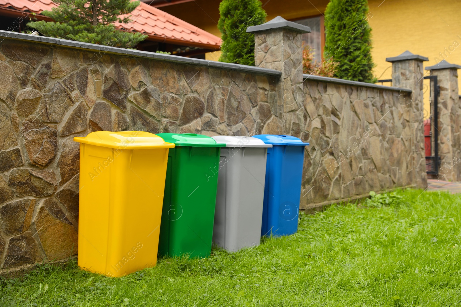 Photo of Many colorful recycling bins near stone fence outdoors