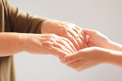 Photo of Helping hands on grey background, closeup. Elderly care concept