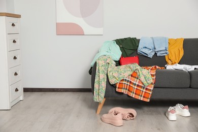 Photo of Messy pile of clothes on sofa and shoes in living room, space for text