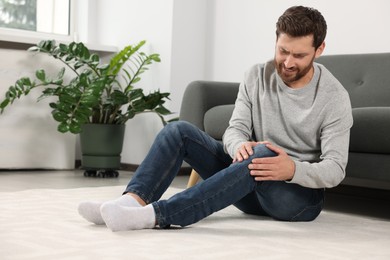 Photo of Man suffering from leg pain near sofa in room