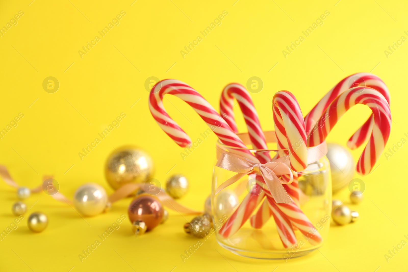 Photo of Candy canes and Christmas balls on yellow background, space for text