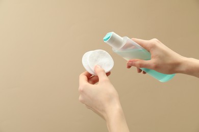 Photo of Woman pouring makeup remover onto cotton pads on beige background, closeup. Space for text