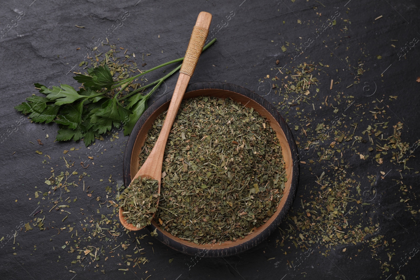 Photo of Plate and spoon with dried parsley on black table, flat lay