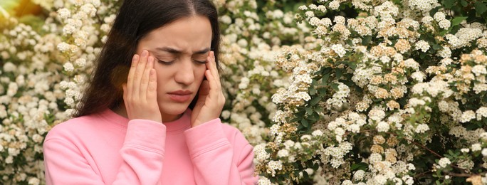 Image of Woman suffering from seasonal pollen allergy near blossoming tree on spring day. Banner design with space for text