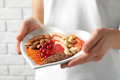 Photo of Woman holding plate with products for heart-healthy diet, closeup